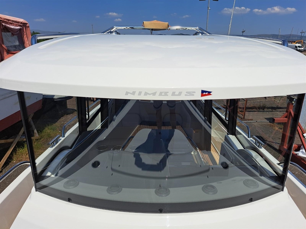 View of a Nimbus boat's top with a sleek white roof and large windshield, showcasing the deck layout and marine environment.